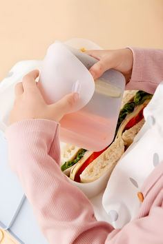 a person pouring water into a container with a sandwich in front of them on a table