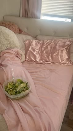 a bed covered in pink sheets and pillows with a bowl of food on the edge