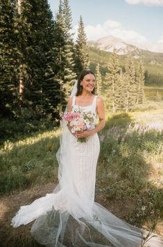 a woman in a wedding dress is standing on the side of a hill holding flowers