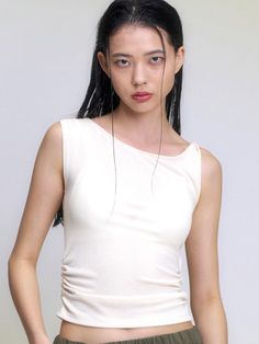 a woman with long black hair wearing a white top and green pants is looking at the camera