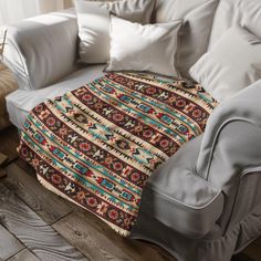 a couch with a blanket on top of it next to pillows and a chair in the background