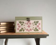 a pink and green box sitting on top of a wooden table next to stack of books