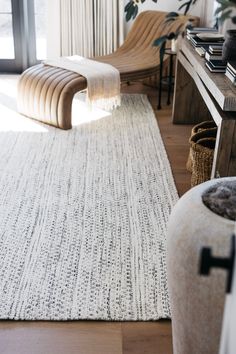 a living room with a rug, chair and plant on the floor in front of a window