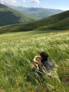 a person sitting in the grass with mountains in the background