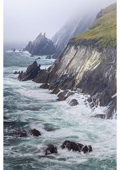 the ocean is choppy and blue with white foamy waves crashing against the rocks