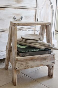 a stack of books sitting on top of a wooden stool next to a dresser with drawers