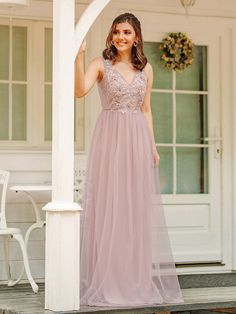 a woman in a long pink dress standing on the porch with her hand up to her face