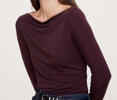 a woman with her hands on her hips wearing a purple shirt and black belted jeans