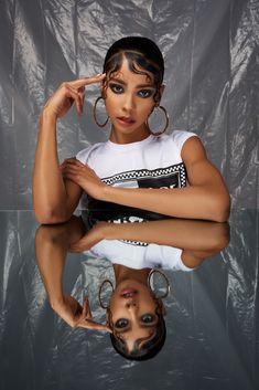 a woman is posing with her hands on her head and wearing large hoop earrings in front of a gray background