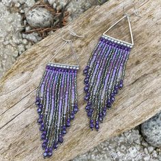 purple and silver beaded fringe earrings on wooden plank with rocks in the back ground