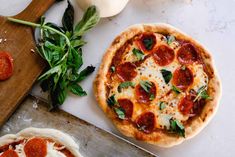 two pizzas sitting on top of a wooden cutting board next to vegetables and cheese