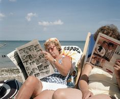 two women sitting on the beach reading newspapers