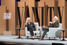 two people sitting in chairs talking on stage