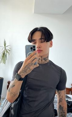 a man with tattoos taking a selfie in front of a mirror while holding a cell phone