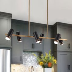 three lights hanging from the ceiling in a kitchen with gray cabinets and stainless steel appliances