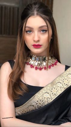 a woman wearing a black and gold sari with red beads on her neck, posing for the camera