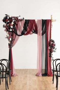 an arch decorated with flowers and ribbons in front of a wooden floored room filled with black chairs