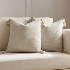 two pillows sitting on top of a couch with tasselled edges and fringe trim