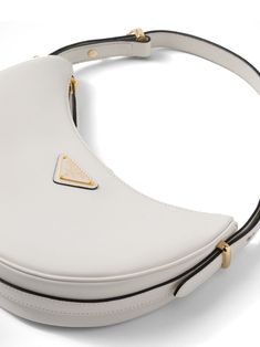 Find PRADA Arqué Leather Shoulder Bag on Editorialist. This Prada shoulder bag is crafted from white leather. It features gold-tone hardware, an enamel triangle logo, an adjustable shoulder strap, a top zip fastening, and a main compartment. White Calf Leather Shoulder Bag With Removable Pouch, Designer White Calf Leather Shoulder Bag, Luxury White Calf Leather Shoulder Bag, Prada Shoulder Bag, Triangle Logo, White Bag, White Leather, Leather Shoulder Bag, Prada