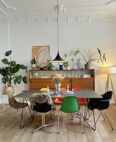 a dining room table with chairs and plants in the corner next to it on top of a hard wood floor