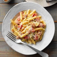 a white plate topped with pasta covered in meat and cheese on top of a wooden table