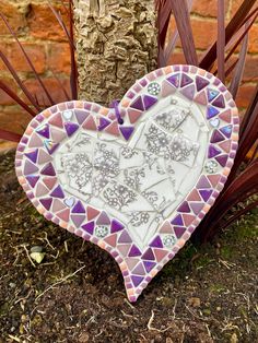 a heart shaped mirror sitting next to a tree in front of a brick wall and grass