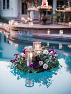 candles are placed in the middle of a pool with flowers and greenery on it