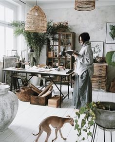 a woman standing next to a dog in a room with plants on the walls and floor