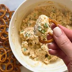 a hand holding a pretzel in a bowl filled with dip surrounded by pretzels