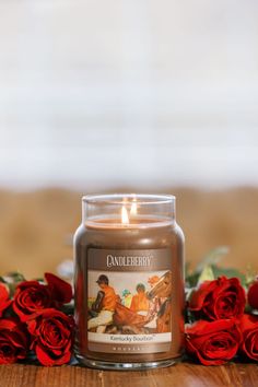 a candle sitting on top of a wooden table next to red roses