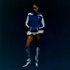 a woman in short shorts and knee high boots standing on a blue background with her arms behind her back