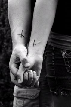 two people holding hands with cross tattoos on their arms and one is holding the other's hand