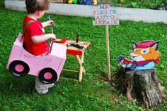 a little boy that is sitting in front of a fake car with a sign saying mr fix's auto repair