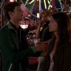 two people standing next to each other in front of carnival rides and ferris wheel at night