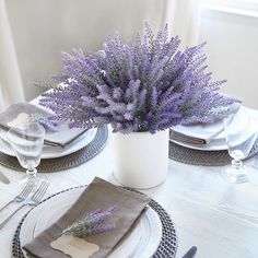 the table is set with place settings, silverware and purple flowers in a white vase