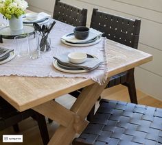 a wooden table topped with black and white place settings next to a vase filled with flowers