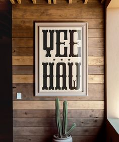 a cactus in a pot with the words yee hau above it on a wood paneled wall