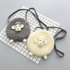 two sheep shaped purses sitting on top of a white and gray mat with black straps