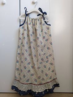 "Your child will feel cool and comfortable all summer long in this loose fitting sundress with adjustable tie straps. This dress features a small patch pocket on the front of the dress, a ruffled hem, and a lovely navy and cream floral pattern. This dress is fully lined, as the main fabric is very lightweight. This listing is for the navy and cream sundress as shown in the thumbnail. The blue check dress on the model is only to show the fit of the dress. This dress is listed as size 5-7, but ple Vacation Cotton Sundress With Ruffled Straps, Cotton Sundress With Ruffled Straps For Vacation, Cute Sundress With Ruffled Straps For Vacation, Summer Cotton Sundress With Ruffled Straps, Casual Cotton Sundress With Ruffled Straps, Cotton Sundress With Tie And Ruffled Straps, Cute Sundress With Tie Straps For Vacation, Cotton Sundress With Tie Back And Ruffled Straps, Cute Sundress With Ruffled Adjustable Straps