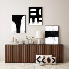 three black and white paintings hang on the wall next to a wooden cabinet with two lamps