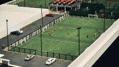 a model of a soccer field with cars parked on the sidelines and people playing