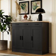 a black cabinet in a living room next to a potted plant and pictures on the wall