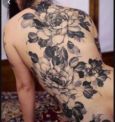 the back of a woman's body with black and white floral tattoos on it