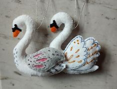 two white swans with orange beaks are hanging from silver chain necklaces on a gray surface