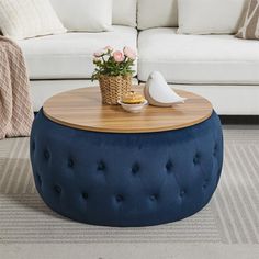 a living room with a white couch, blue ottoman and coffee table in the middle