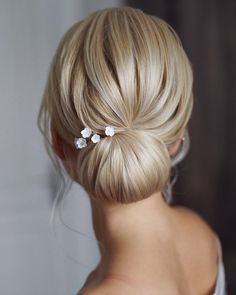 a woman with blonde hair in a low bun with flowers pinned to her side, wearing a white dress