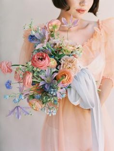 a woman holding a bouquet of flowers in front of her face and wearing a pink dress