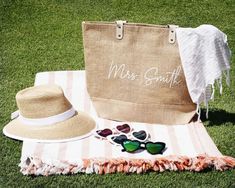 a beach towel, hat, sunglasses and tote bag sitting on the grass