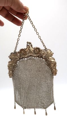 a hand holding a silver purse with chains hanging from it