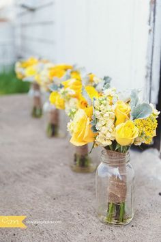 yellow flowers are in mason jars lined up on the side of a barn window sill